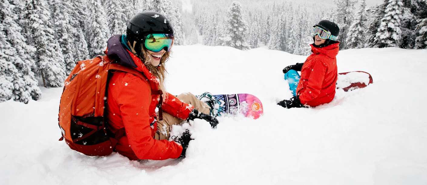 Twee snowboarders in de poedersneeuw tussen besneeuwde naaldbomen