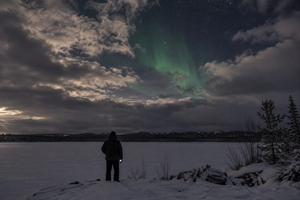 Reiziger kijkt naar een deels bewolkte hemel met zwak noorderlicht in Fins Lapland