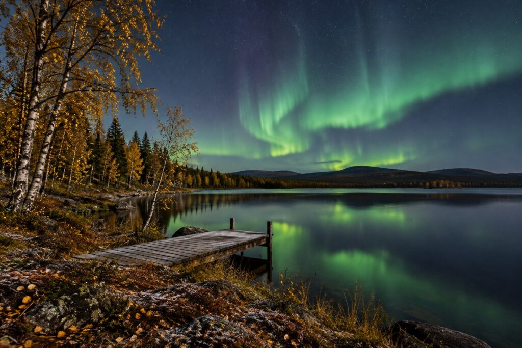 Noorderlicht weerspiegelt boven een meer met berken in herfstkleuren in Fins Lapland